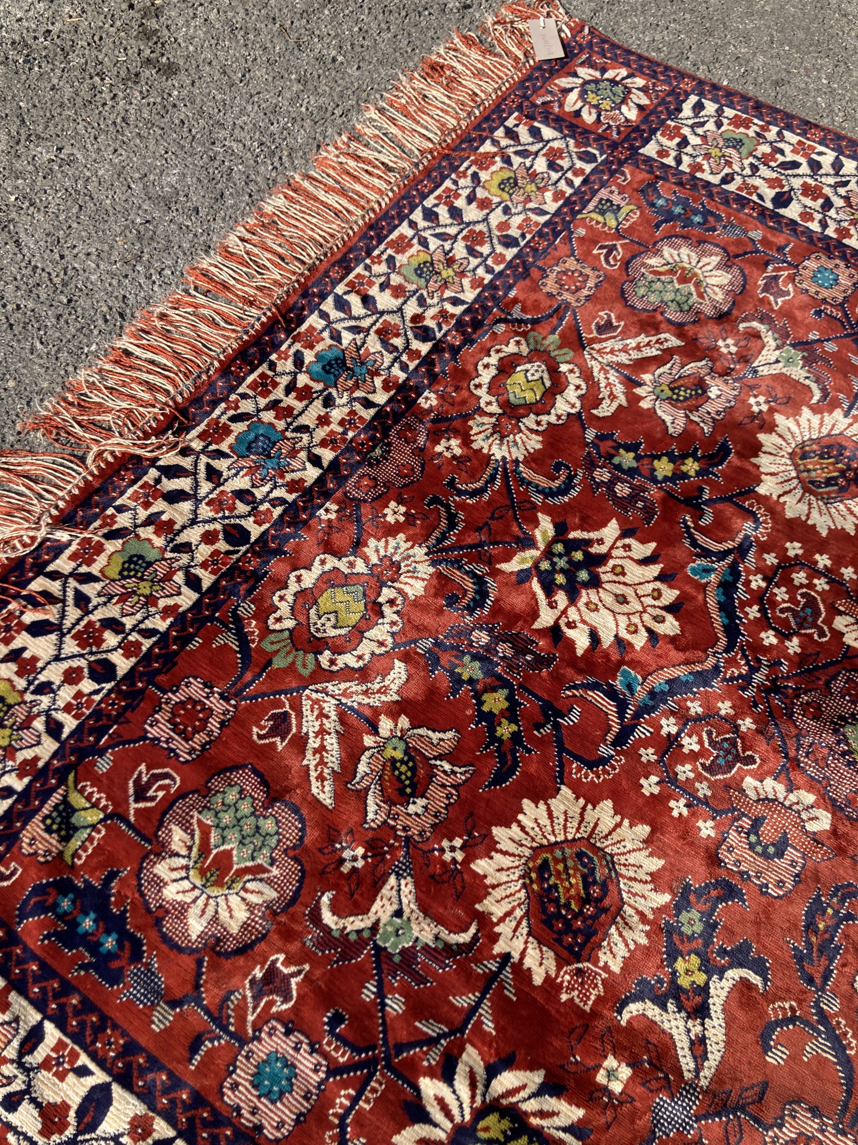 A large embroidered silk rug with a claret red ground interspersed with symmetrical foliate decoration, 136 x 260cm